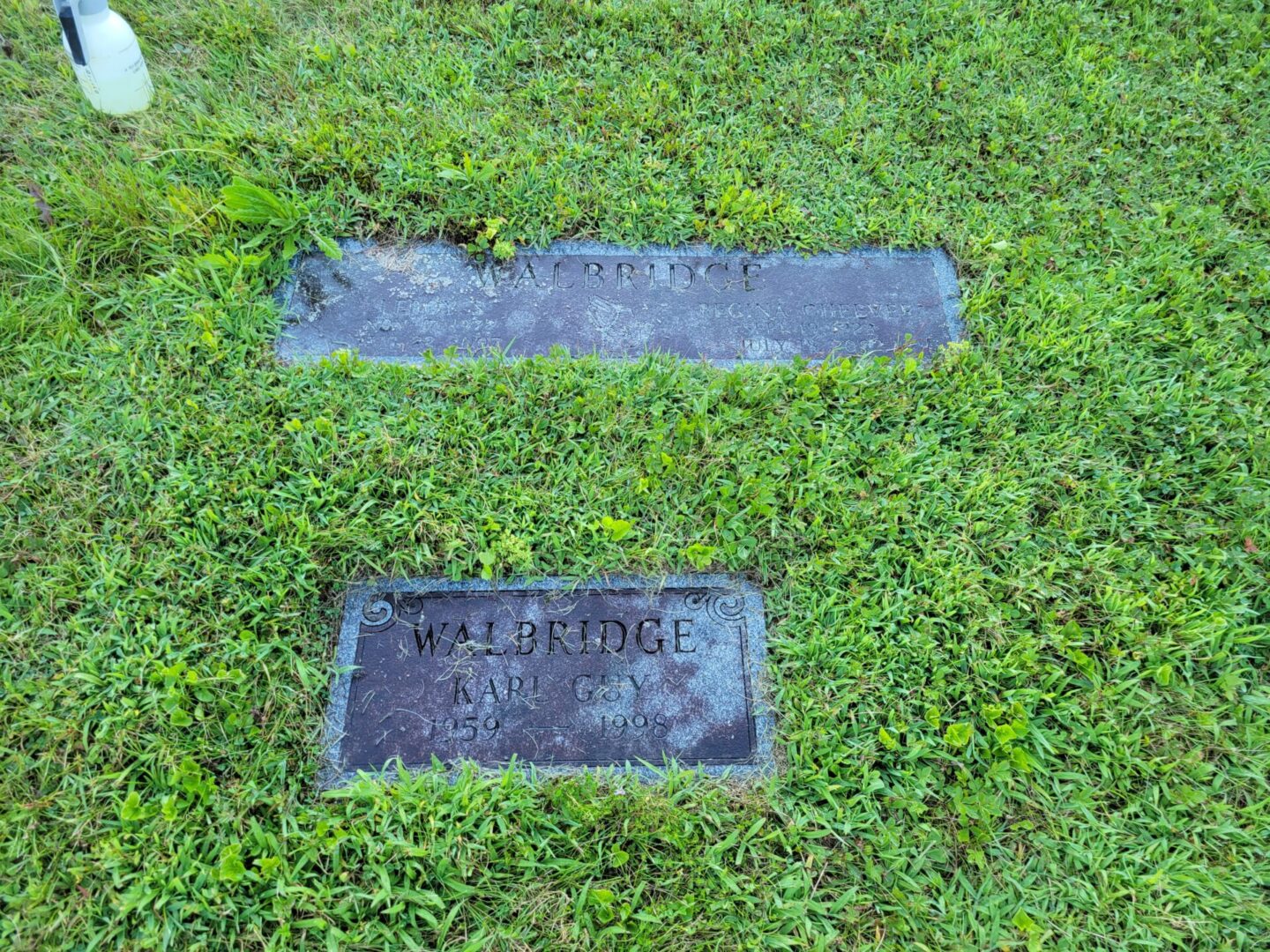Two grave markers in the grass with a name and address.