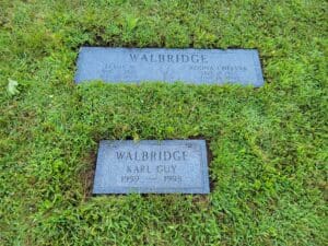 Two grave markers in the grass with a name and date of birth.