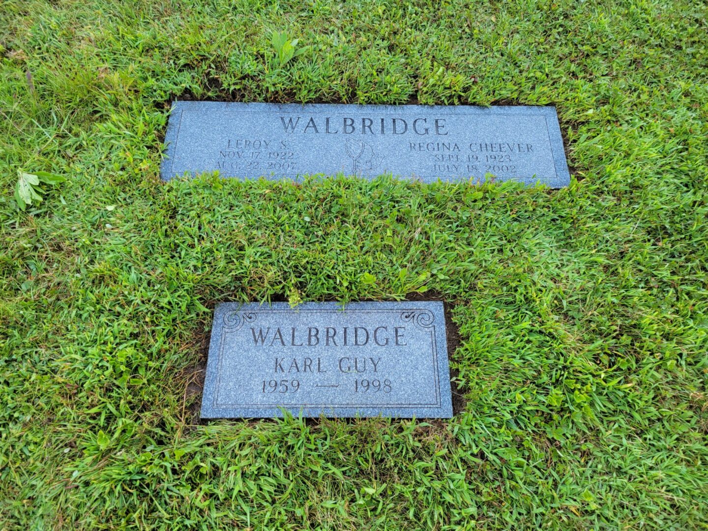 Two grave markers in the grass with a name and date of birth.